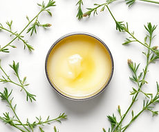 white background, ointment in tin with green herbs around it.jpg