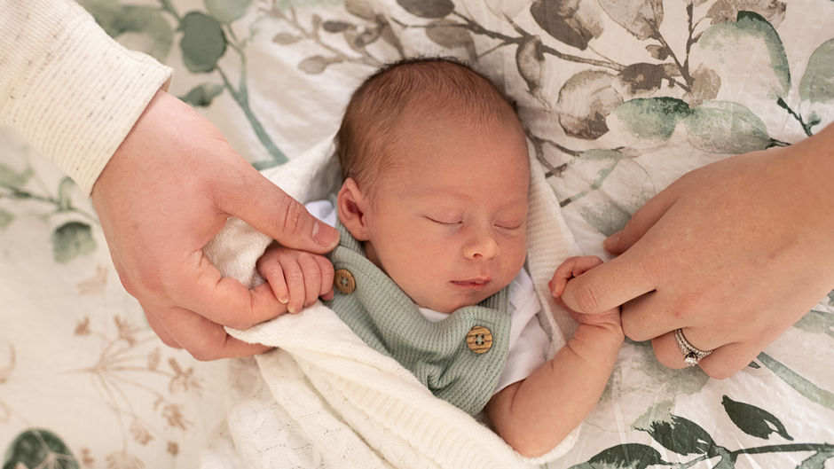 Newborn baby sleeps in his home while holding each of his parents hands. Wilmington, DE newborn photographer
