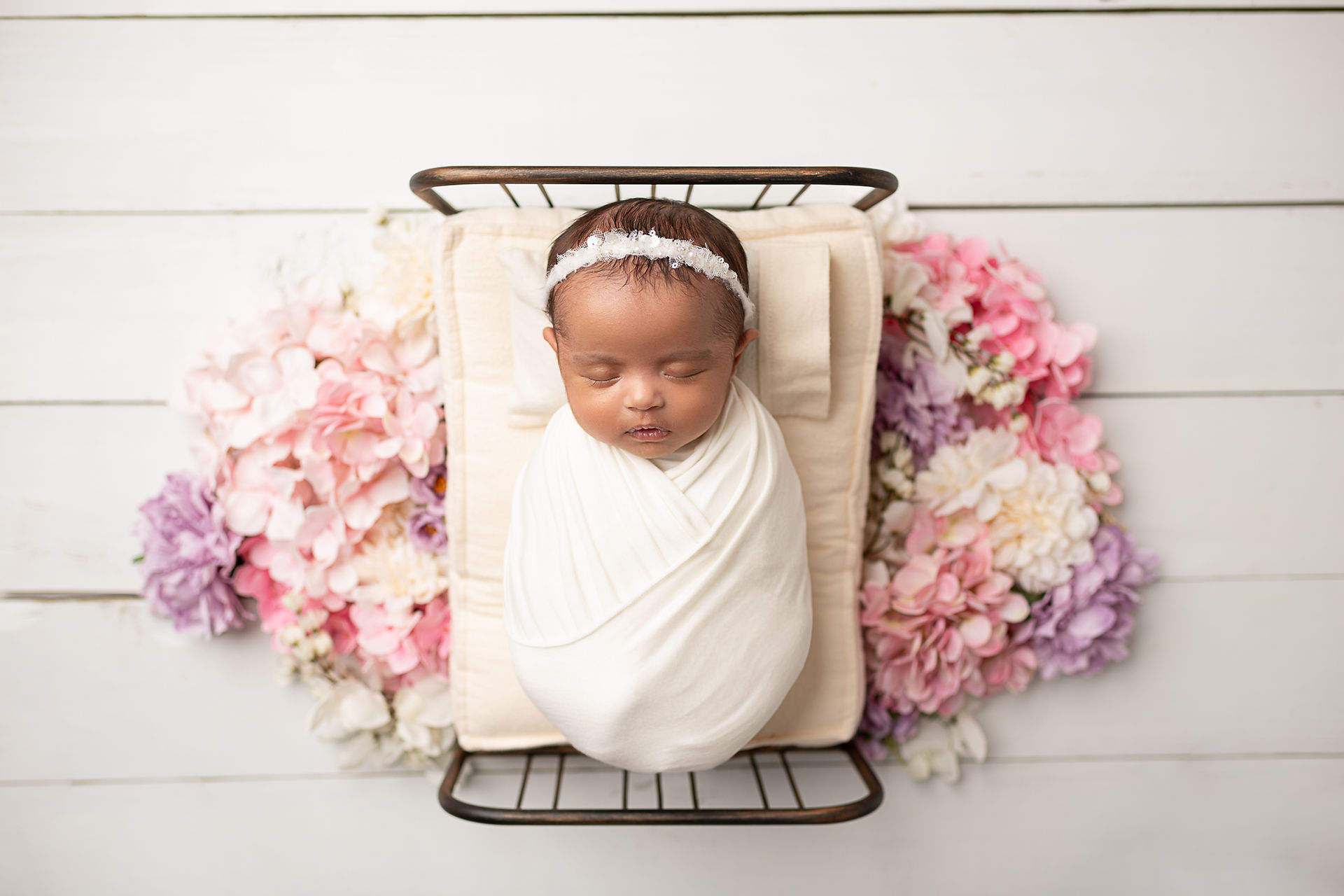 Twin girl sleeps on a bed with flowers around her. Newborn photo studio delaware