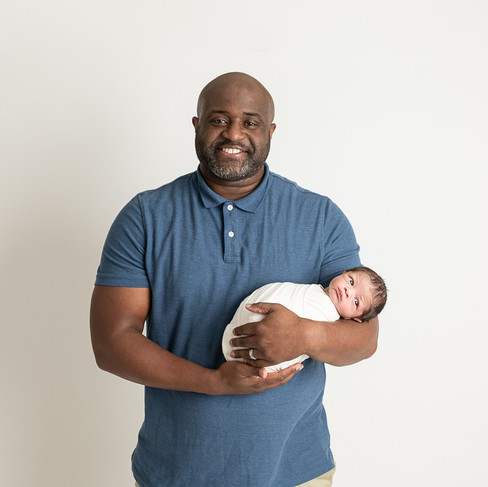 Dad smiles while holding newborn baby boy wrapped in white. Wilmington, DE photostudio