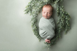 infant smiles wrapped in green with greenery around him