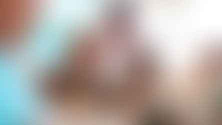 Professor interage com grupo diverso de crianças em sala de aula iluminada. Todos estão sentados à mesa usando tablets, em um ambiente colaborativo e tecnológico. Ao fundo, há um quadro de avisos colorido com cartazes.