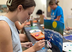 girl painting a picture in a classroom setting. You see others in the background.