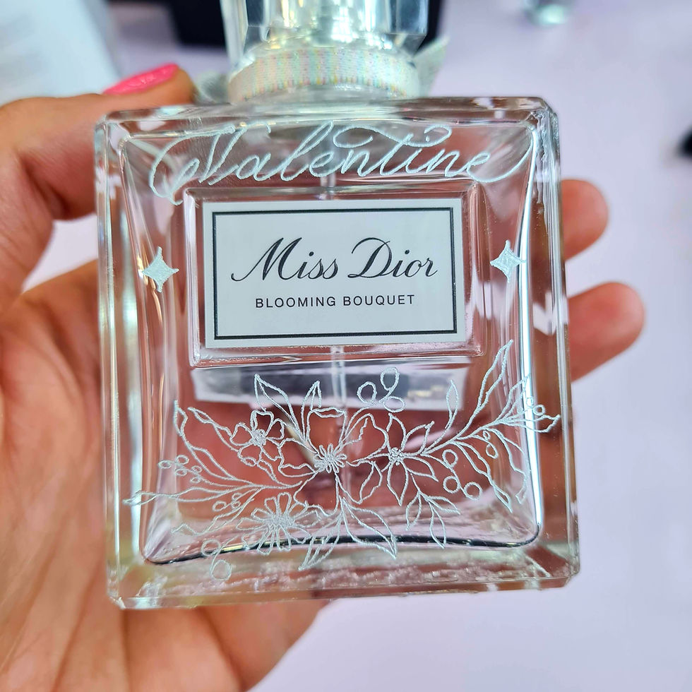Flacon de parfum Miss Dior tenu en main, fond rose. Design floral, prénom gravé, et texte "Blooming Bouquet" visibles sur le flacon transparent.