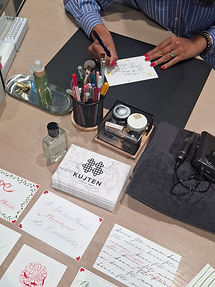 Une personne écrit sur une carte décorée d'étoiles, entourée de fournitures colorées et cartes calligraphiées sur un bureau en bois.