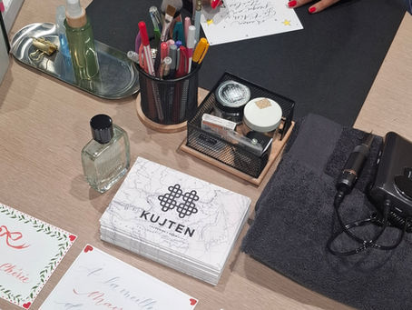 Une personne écrit sur une carte décorée d'étoiles, entourée de fournitures colorées et cartes calligraphiées sur un bureau en bois.