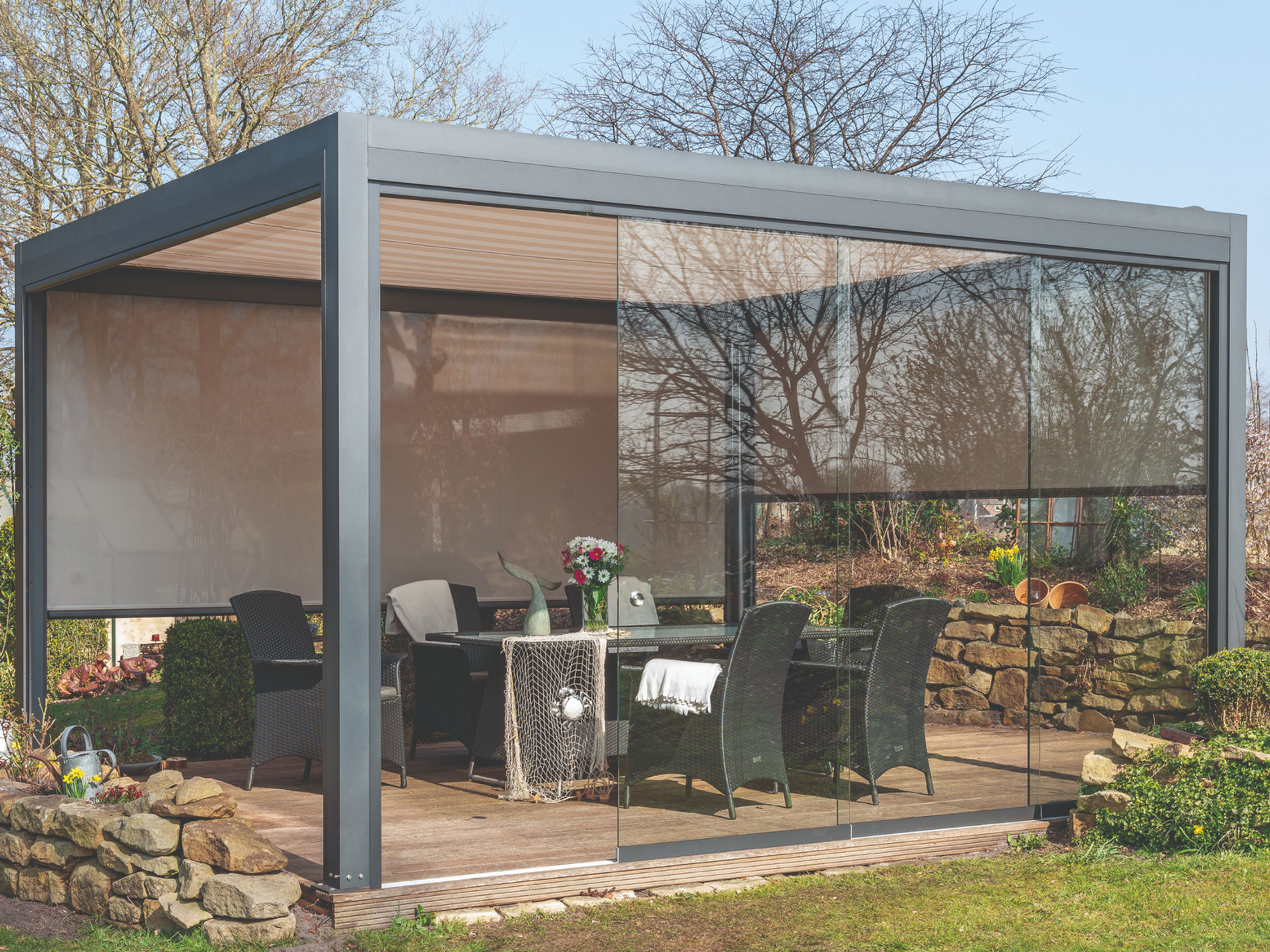 Freistehende Aluminium-Pergolamarkise mit textiler Horizontalbeschattung auf einer Holzterrasse mit Esstisch im Grünen, moderne kubische Bauform von formkonzept Outdoor Solutions NRW