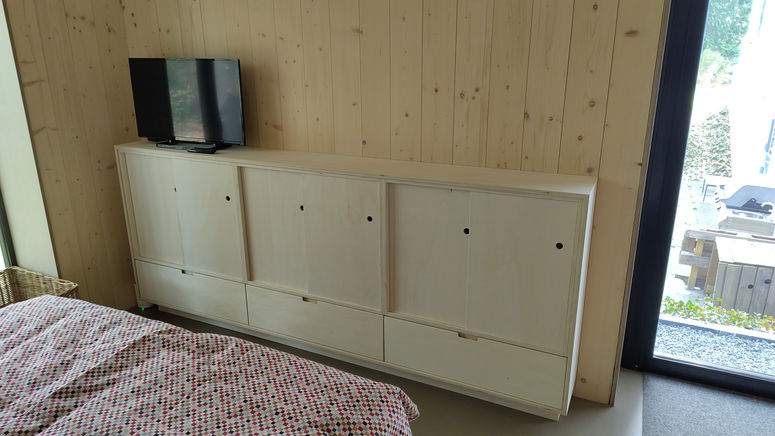 slaapkamerkast met schuifdeuren en lades gemaakt van populierenplex met een tv bovenop. deuren zijn dicht