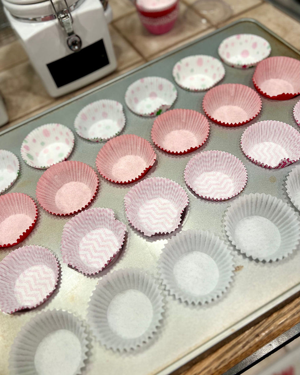 A prepared cupcake pan, four rows with a different color oc cupcake liner per each row, on a counter.