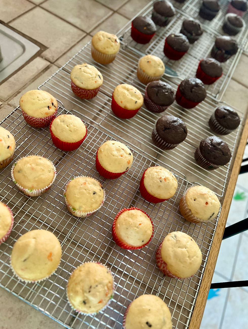 3 wire cooling rack on a tile counter with freshly baked vanilla and chocolate funfetti cupcakes on them.