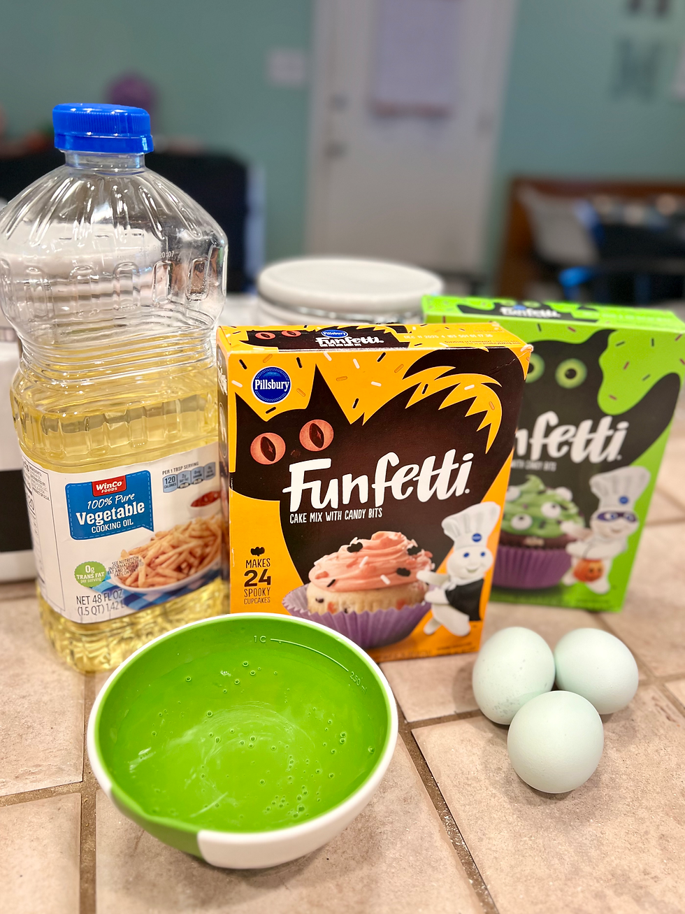 A collection of cupcake baking supplies. Funfetti cake mix, oil, water, and eggs on a counter.