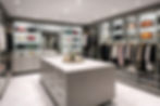 Luxurious custom VelArt walk-in closet with handbags, clothes on racks, and a central island. Bright lighting, sleek design, and marble flooring.