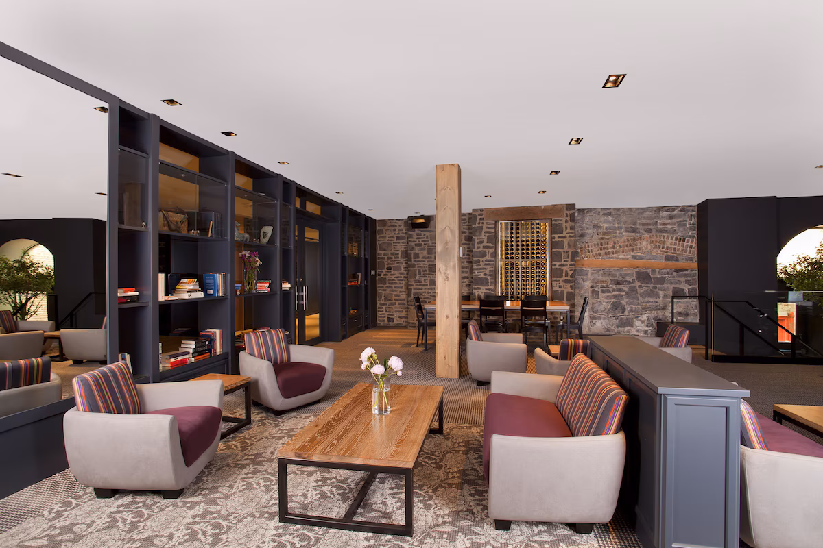 Lobby of Hôtel du Vieux‑Québec in Old Quebec City featuring cozy seating, stone walls, a fireplace, library shelves, and warm lighting creating a welcoming boutique atmosphere.