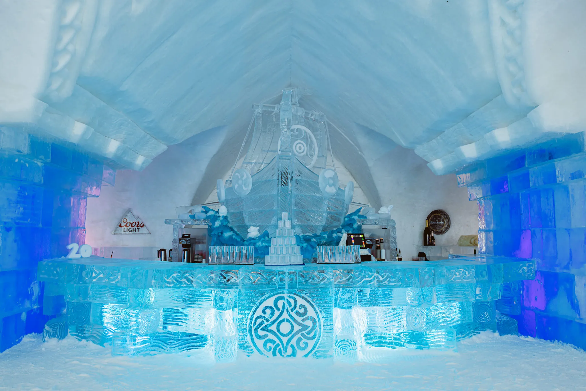 ce Bar at Hôtel de Glace near Quebec City, built entirely of ice and snow, featuring sculpted walls, glowing colored lights, and cocktails served in glasses made of ice.
