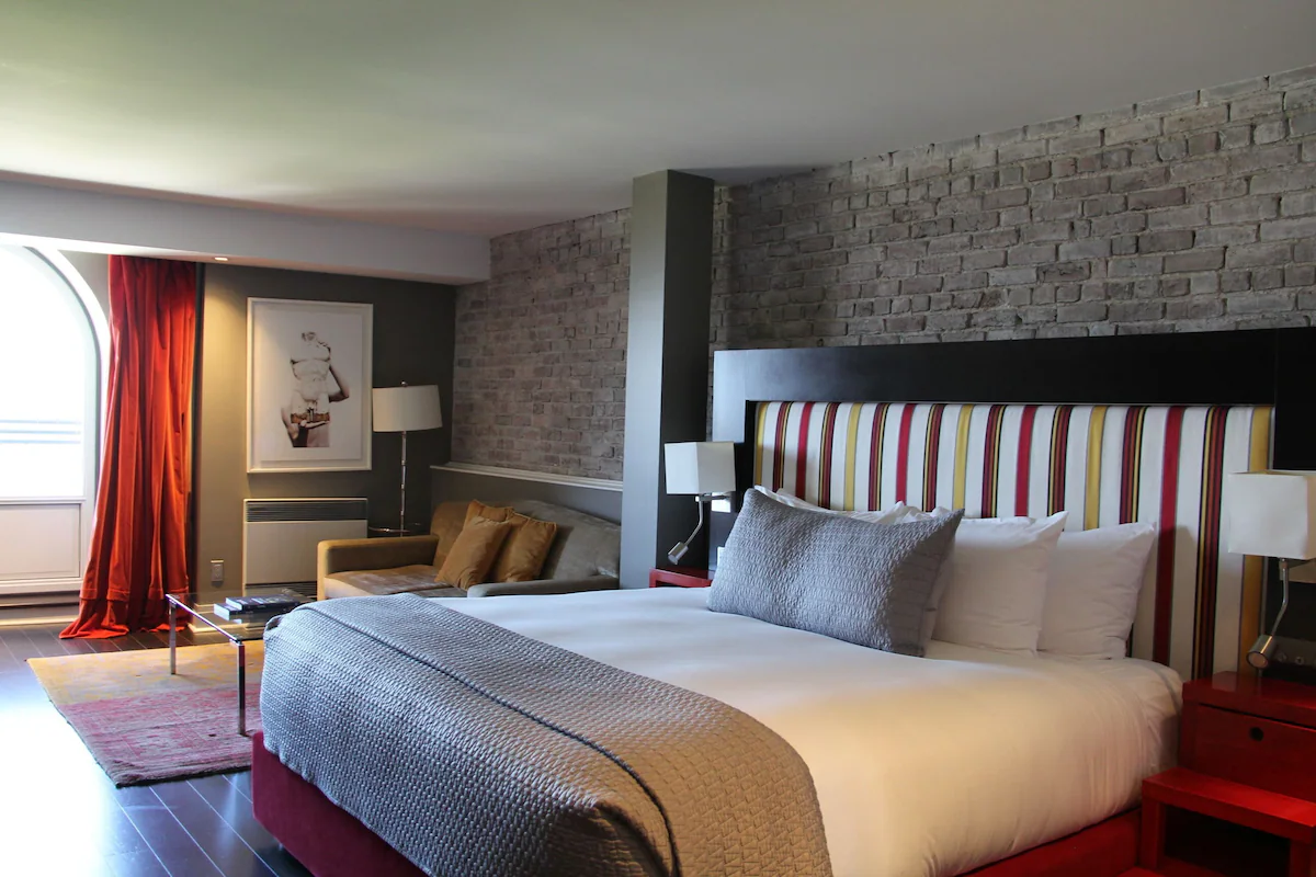 Guest room at Auberge Saint-Antoine in Quebec City featuring contemporary décor, plush bedding, curated historic artifacts, and large windows with views of the Old Port or St. Lawrence River.