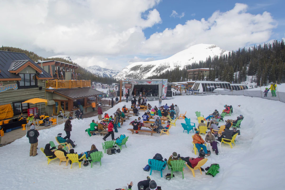 Outdoor firepits at Sunshine Mountain Lodge in Banff National Park, Alberta, glowing against the snow in winter, surrounded by Adirondack chairs and framed by alpine peaks and evergreen forest.