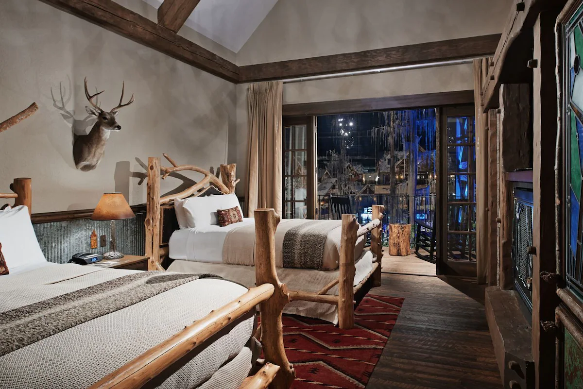 Guest room at Big Cypress Lodge in Memphis, Tennessee, featuring rustic‑luxury décor with handcrafted wood furniture, stone accents, an electric fireplace, and views of the Mississippi River or the Pyramid’s cypress‑themed interior.
