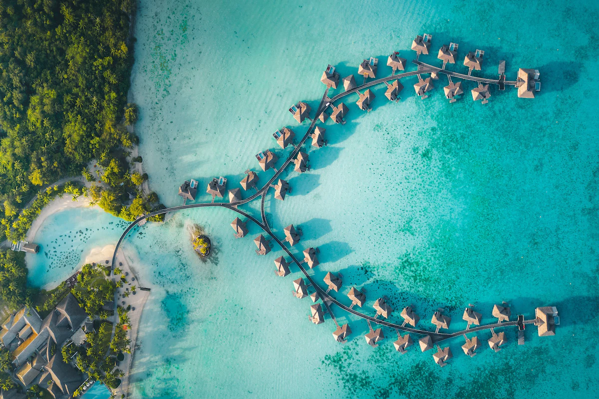 Aerial view of InterContinental Le Moana Bora Bora Resort with overwater bungalows extending into the turquoise lagoon, set against Matira Point and Mount Otemanu.