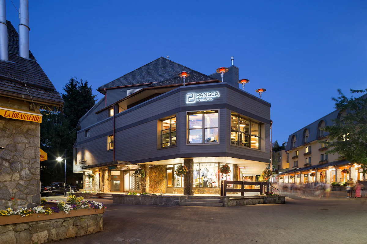 Exterior of Pangea Pod Hotel in Whistler Village, featuring a modern, minimalist façade with large windows, warm lighting, and inviting street‑level café entrance.