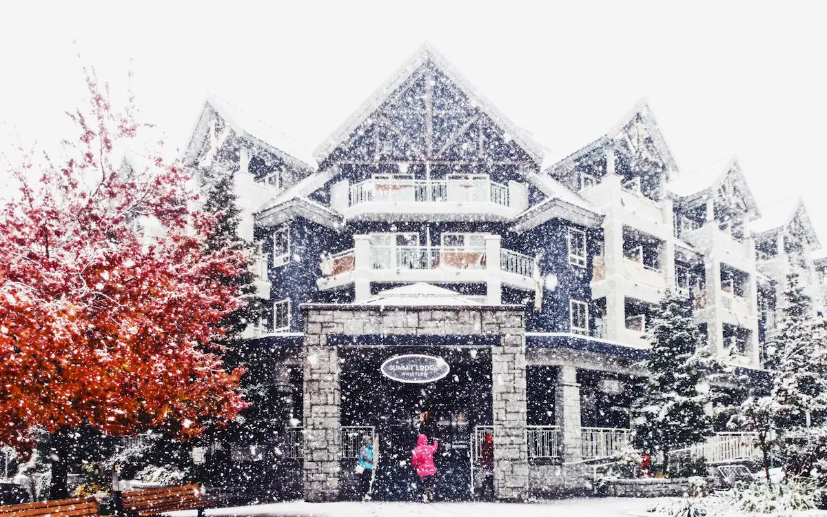 Exterior of Summit Lodge Boutique Hotel in Whistler, featuring alpine lodge architecture with stone façade, pitched rooftops, and a welcoming boutique entrance tucked along Main Street in Whistler Village.