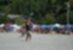 A man is coaching stick game players on the beach. Vendor tents from the Salmon Festival are in the background.