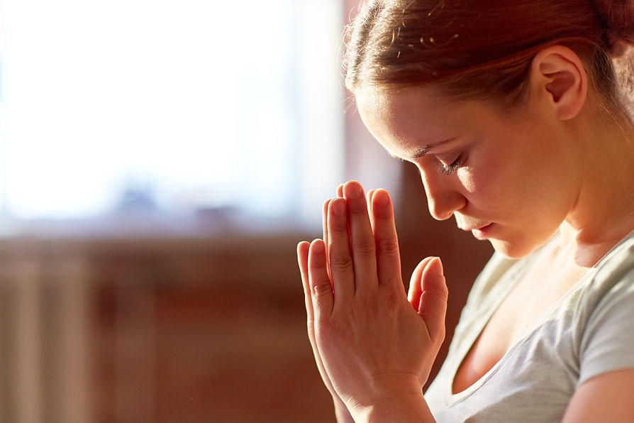 Young woman with eyes closed and hands in prayer position, symbolizing faith, reflection, and inner healing.