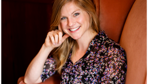 Allie sitting in an rust colored arm chair smiling.