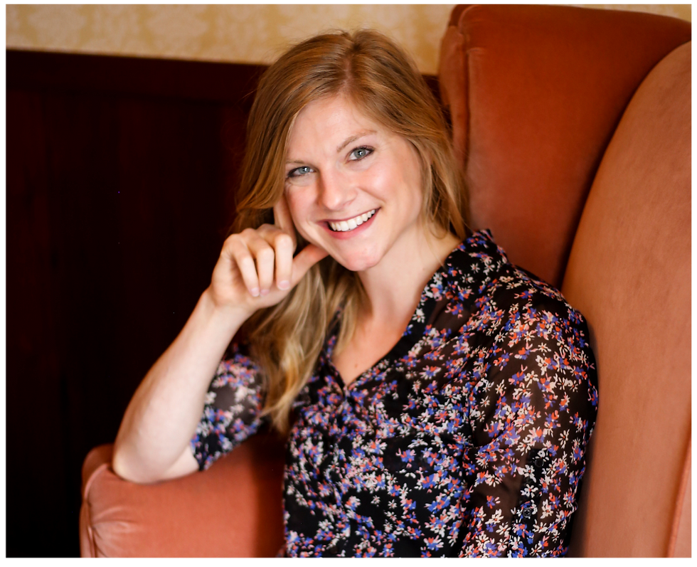 Allie sitting in an rust colored arm chair smiling.