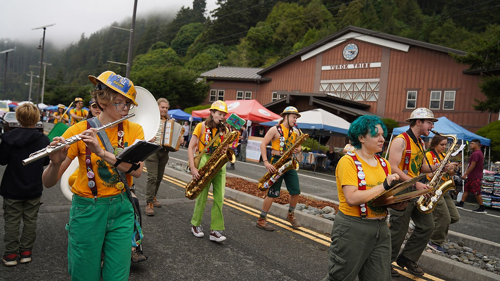 Band in colorful outfits plays instruments, marching on a street with tents and a building in the backdrop on a cloudy day. Joyful mood.
