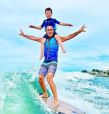 A father and son in an epic pose aboard a surfboard riding the wake behind a yacht.