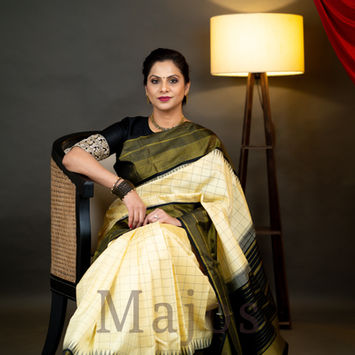Woman in cream and green pure silk saree sitting in chair