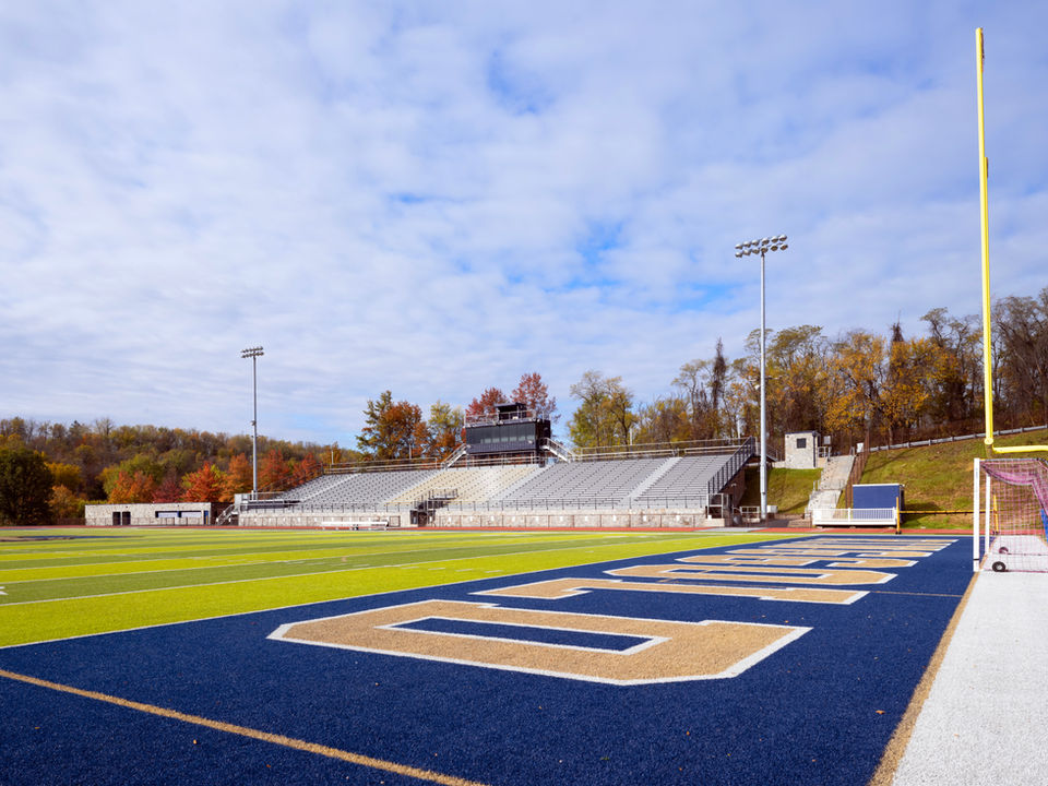Football stadium with blue turf, bleachers, and fall trees