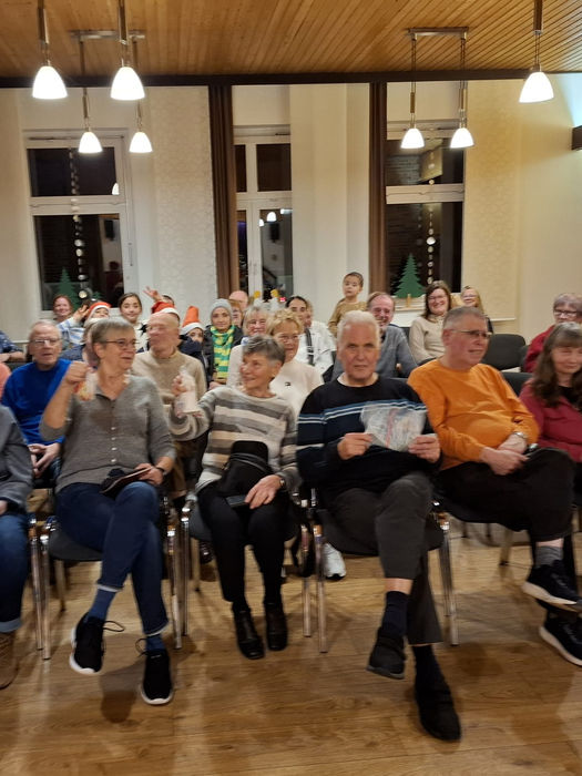 Eine Gruppe von Menschen sitzt auf Stühlen in mehreren Reihen, im Vordergrund steht der Nikolaus. 