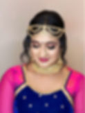 A woman adorned in traditional bridal attire is wearing intricate gold jewelry, including a maang tikka, nose ring, and choke
