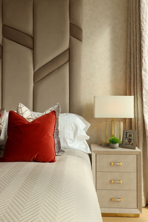 Luxury penthouse bedroom with a geometric upholstered headboard, terracotta accent cushion, and a bedside table with a modern lamp and gold details.
