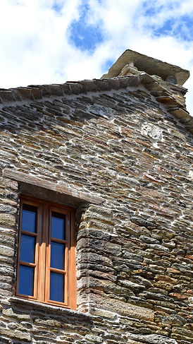 Vue en contre-plongée d'un pignon en schiste avec fenêtre en bois et couronnement de toiture.