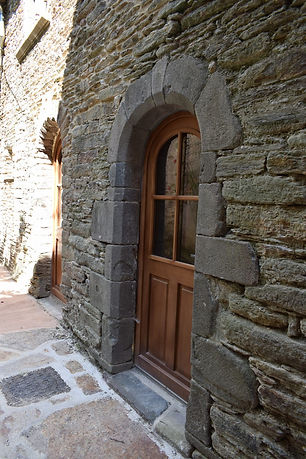 Gros plan sur une porte cintrée en bois vitrée, encadrée de pierres de granit au sein d'une maçonnerie de schiste.