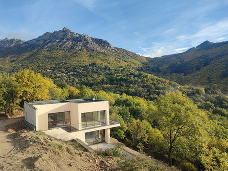 Vue générale de la maison implantée dans la pente au milieu de la végétation automnale. Les rochers de Trenze dominent le paysage et mettent en évidence la relation entre architecture, relief et environnement.