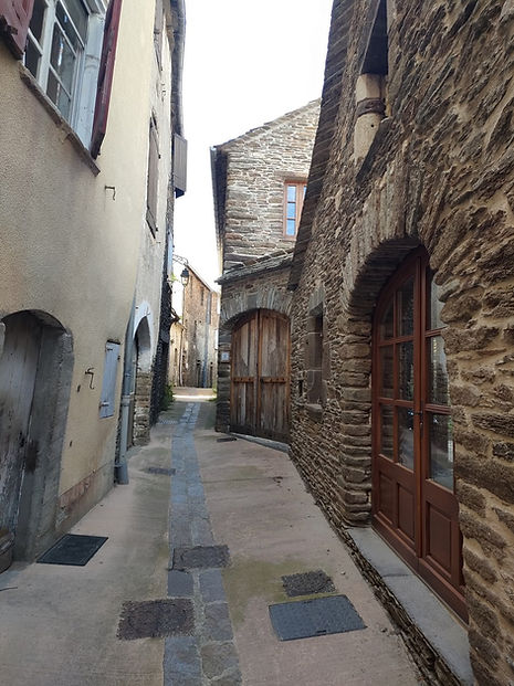 Rue étroite de village avec maison en schiste, porte cintrée vitrée et grand portail ancien.