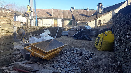 Cour en chantier avec matériaux, gravats, bétonnière et murs en pierre.
