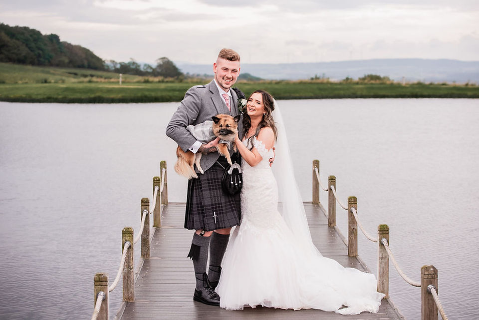 A bride and groom pose with their dog on the pier at The Vu in Bathgate