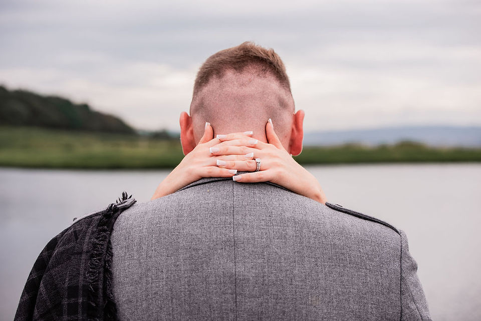 A bride places her hands around her groom's neck with her fingers interlaced and her wedding and engagement rings on show at The Vu in Bathgate
