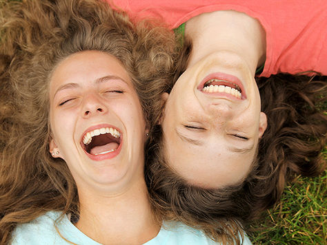 Two teen girls lying in grass laughing 