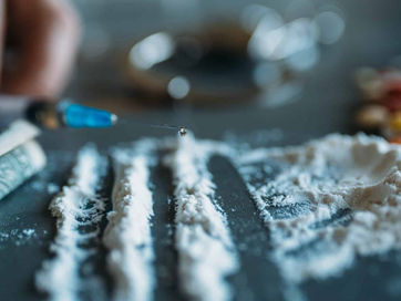 Close-up of white powdered cocaine arranged in lines on a dark surface, highlighting substance abuse and addiction."