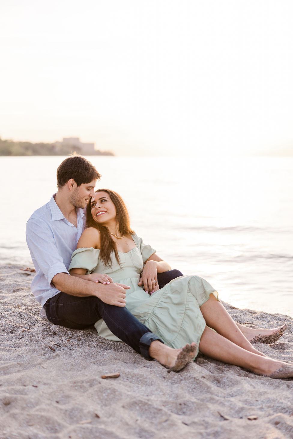 Couple sitting on beach blanket during sunset engagement session with warm golden tones