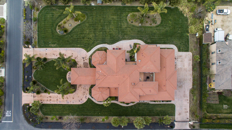 Aerial view of a large house with red tile roof, green lawn, and paths.