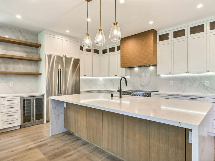 Sleek modern kitchen features large island, stainless steel refrigerator, copper hood, pendant lights.