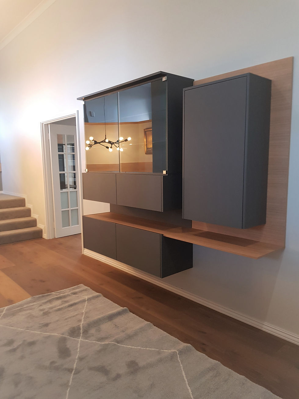 Modern interior with floating dark cabinets, wood accents, and a geometric light fixture. Soft lighting creates a warm atmosphere.