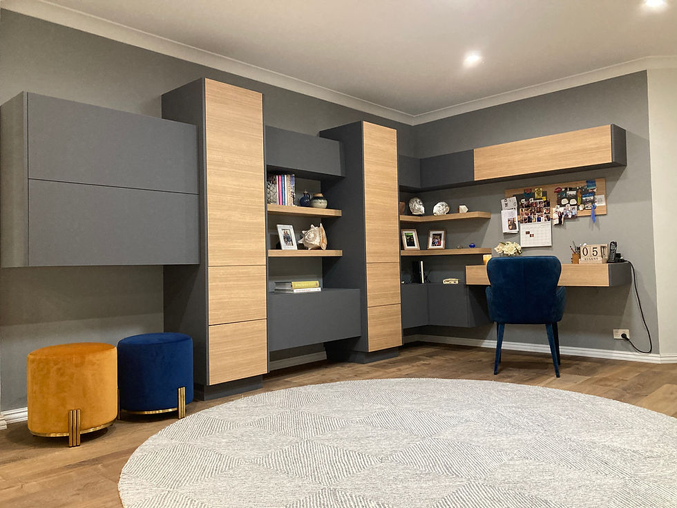 Modern office with gray and wood cabinets, a desk with photos and papers. Blue chair, orange and blue stools, and a round rug on wooden floor.