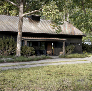 Perspective view of a dark modern cabin and gravel driveway in a forest. By Black Cabin.